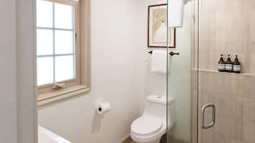 Un baño con inodoro, cabina de ducha de vidrio, ventana y una obra de arte enmarcada en la pared.
