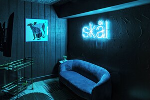Un baño moderno con un letrero de neón que dice "skål", un sofá azul y un cuadro con la imagen de un perro.