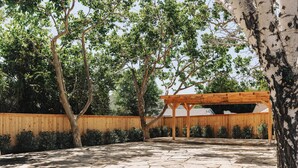An outdoor patio with stone flooring, wooden pergola, and a wooden fence. - The Marlo (Solvang)