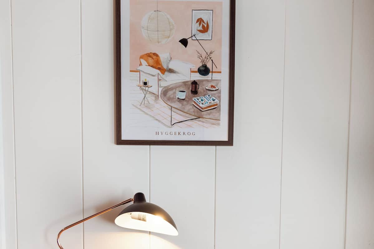 Un pupitre de madera con una silla marrón, una ilustración enmarcada en la pared y una lámpara de escritorio.