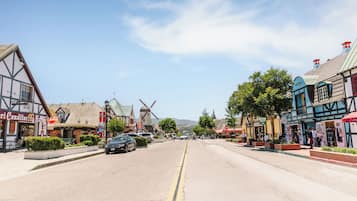 A street lined with traditional half-timbered buildings, a windmill, and parked cars.