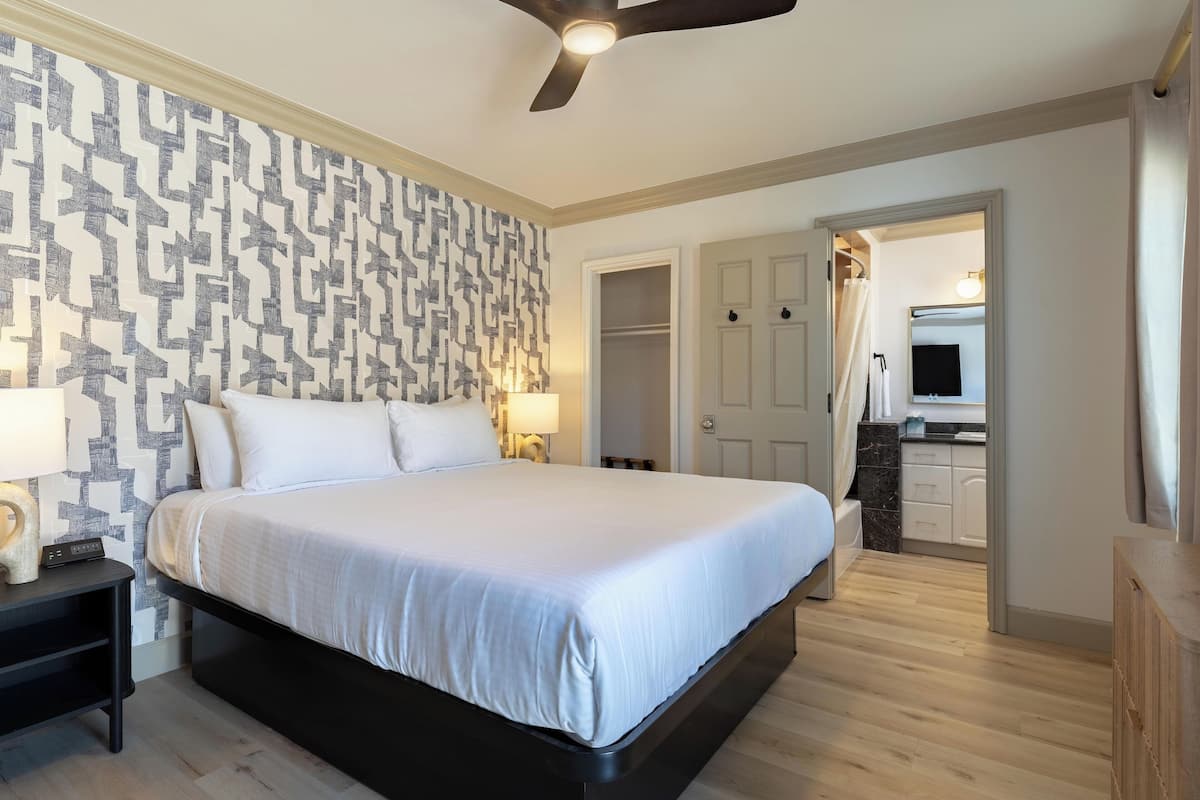 Un dormitorio moderno con una cama grande, ventilador de techo y pared con estampado.