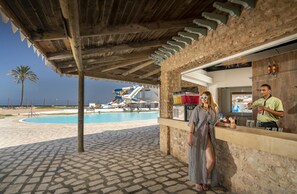 A poolside area with a water slide, a bar, and a person standing by the bar. - Club Sunshine Rosa Rivage - All inclusive (Monastir)