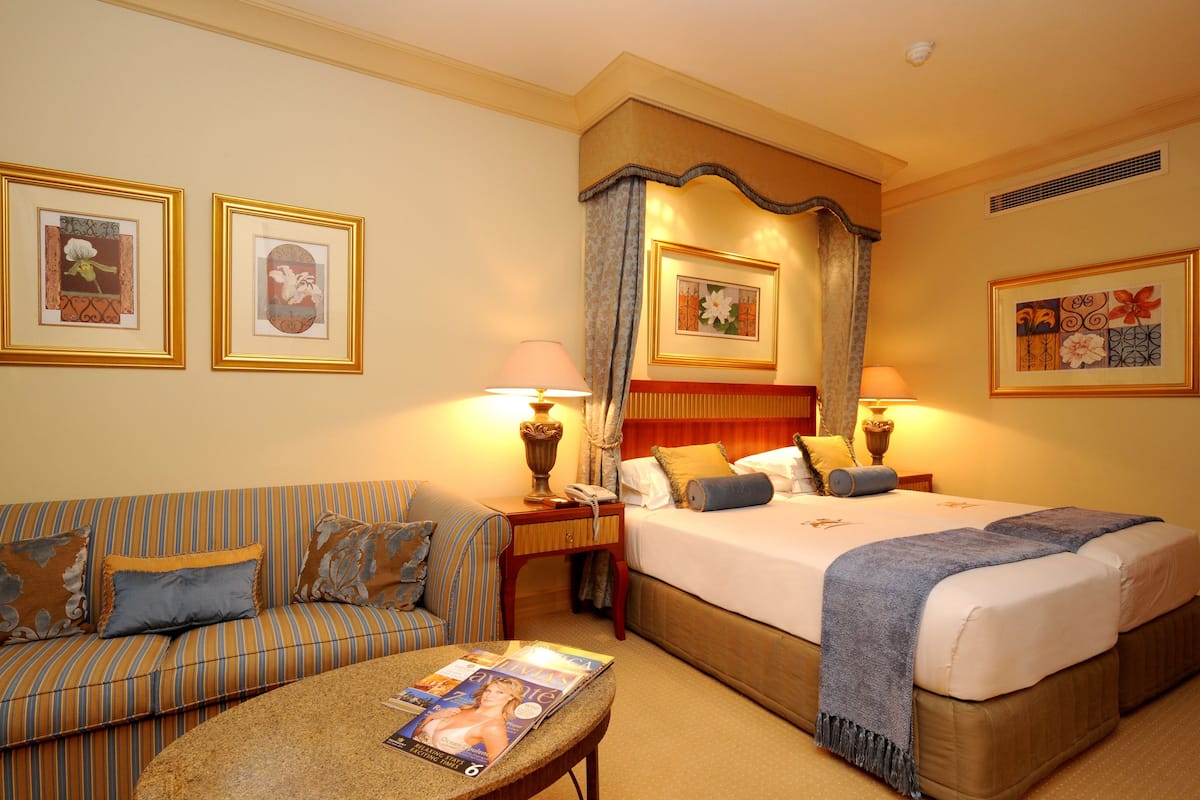 A hotel room with a bed, a sofa, a nightstand, and a table with a magazine.