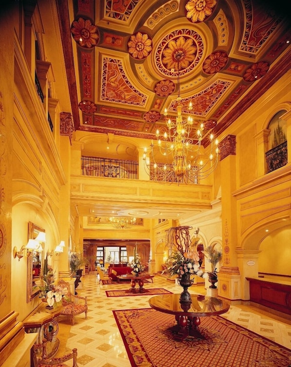 Un vaste hall d’entrée agrémenté de décorations élaborées au plafond, d’un lustre et d’une fontaine centrale.