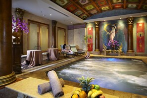 Área de piscina interior luxuosa, com um mural, cadeiras de descanso e uma mesa com toalhas.