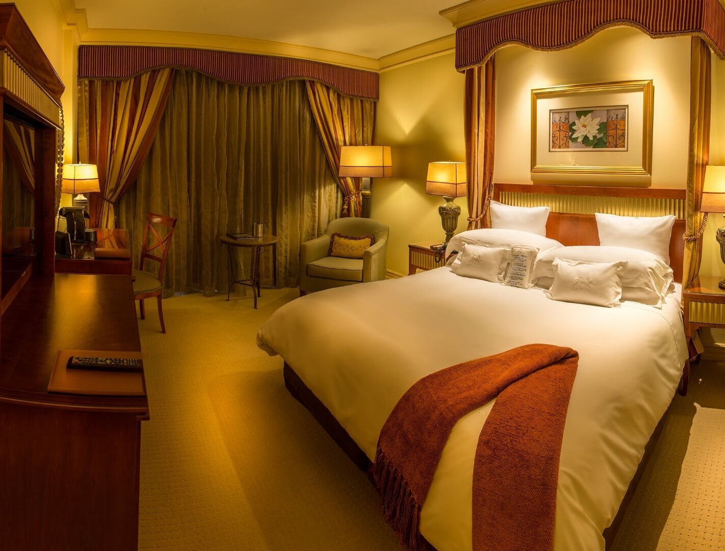 A hotel room with a large bed, two bedside tables, a chair, a desk, and a desk lamp.
