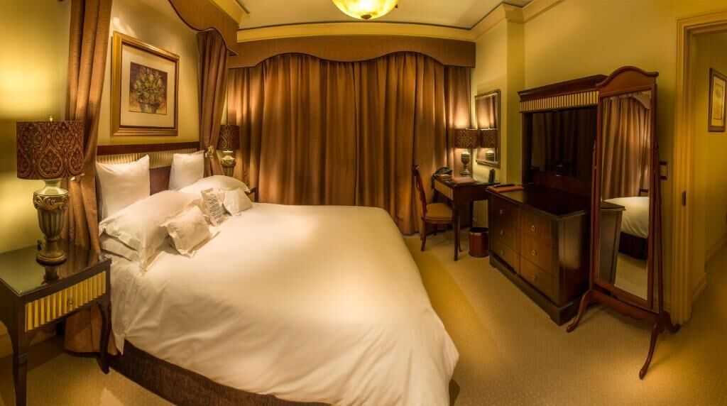A spacious hotel room with a large bed, a desk, a wardrobe, and a mirror.