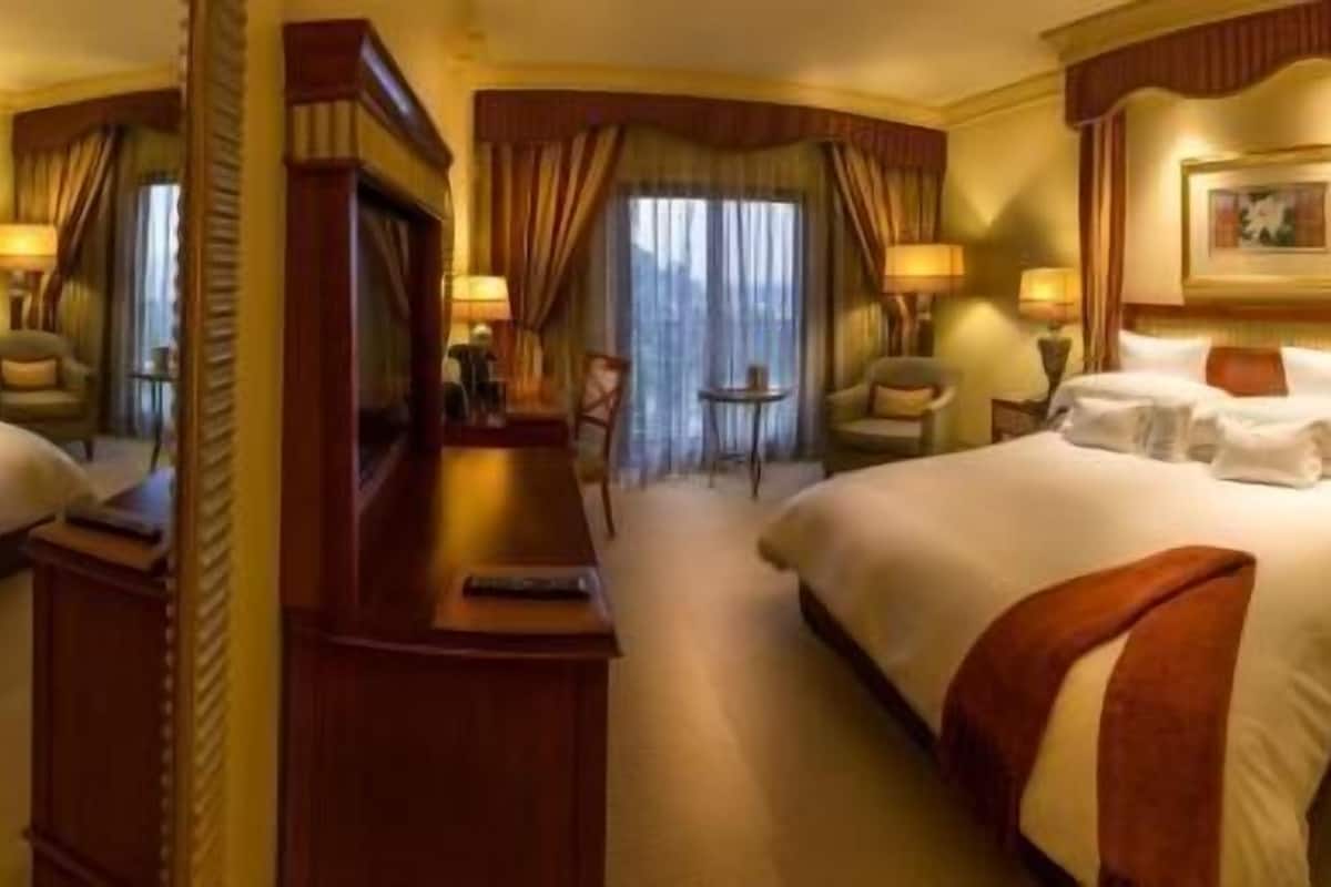 A hotel room with a large bed, a desk, a chair, a small table, and a mirror.