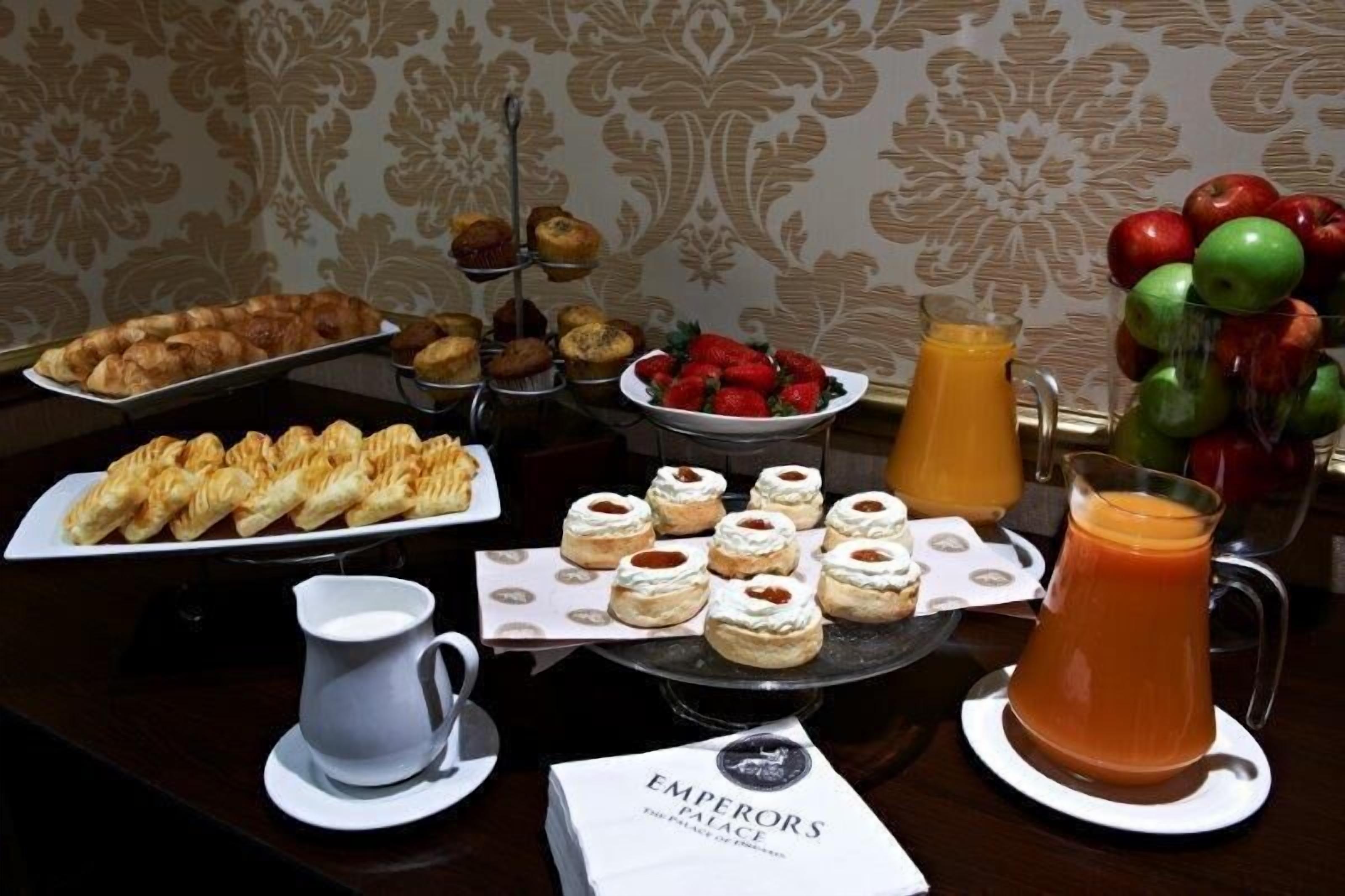 Una mesa de buffet con pastelería, una jarra de jugo de naranja y un plato de fresas.