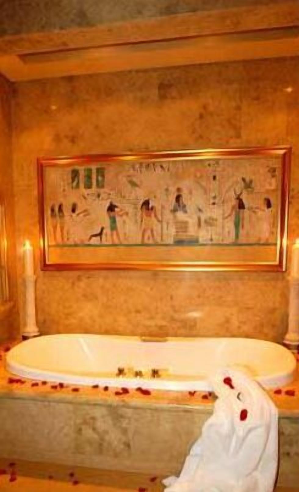 Ein Badezimmer mit einer großen Badewanne, einem Wandbild und einem weißen Handtuch auf dem Boden.