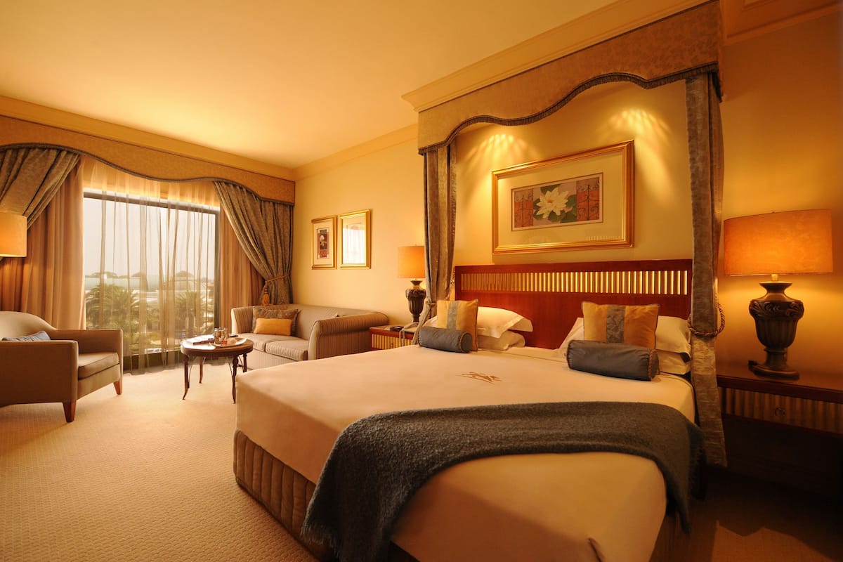 A hotel room with a large bed, two armchairs, a small table, and a view of the outdoors.