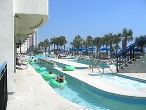 A pool area with multiple lanes for water slides, surrounded by palm trees and umbrellas. - Boardwalk Beach Resort (Myrtle Beach)