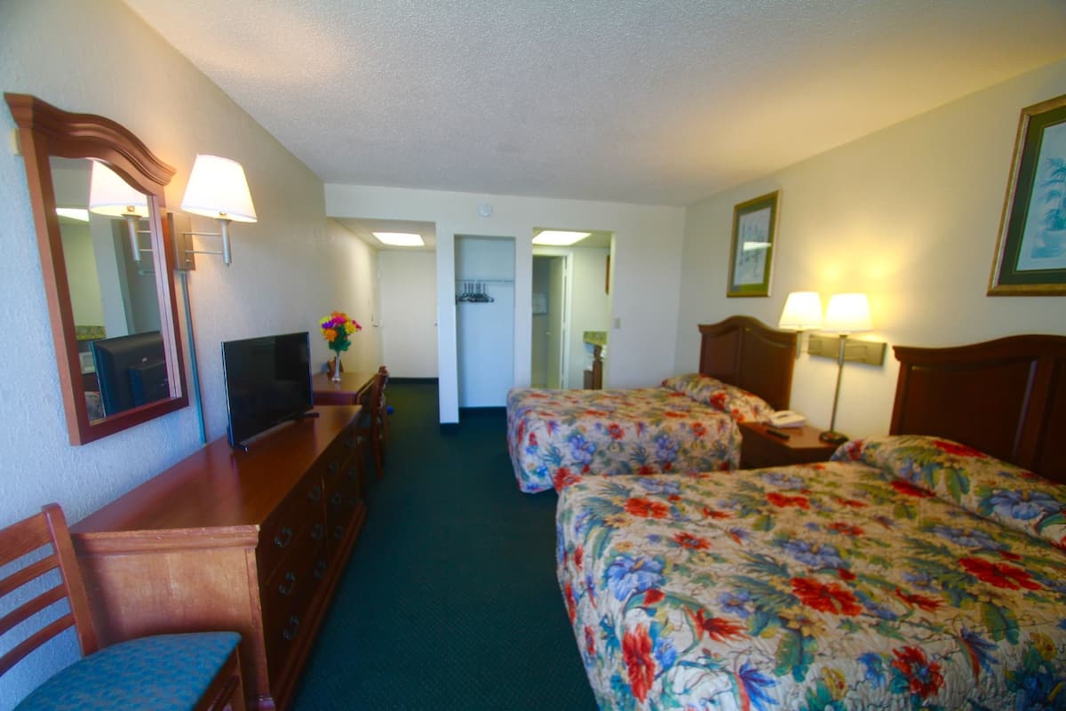 A hotel room with two beds, a desk with a television, a dresser, and a mirror.
