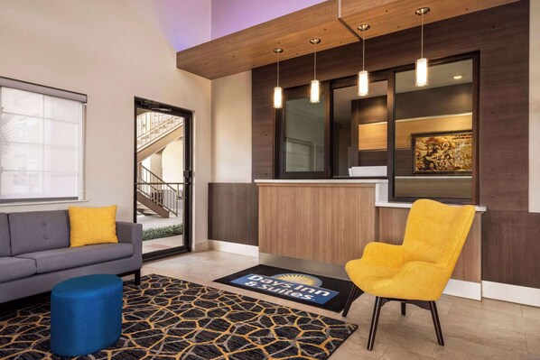 A hotel lobby with a sofa, a yellow armchair, a blue ottoman, a reception desk, and a staircase. - Days Inn & Suites by Wyndham Houston Hobby Airport (Houston)