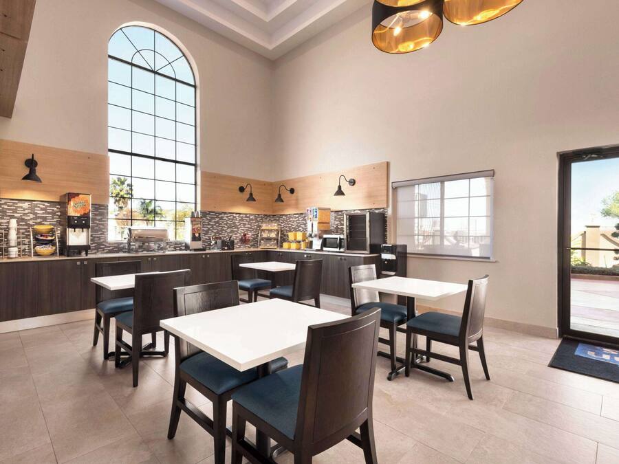 Un restaurante moderno con techos altos, ventanas amplias y paneles de madera en tonos oscuros y claros. Mesas y sillas dispuestas para comer.