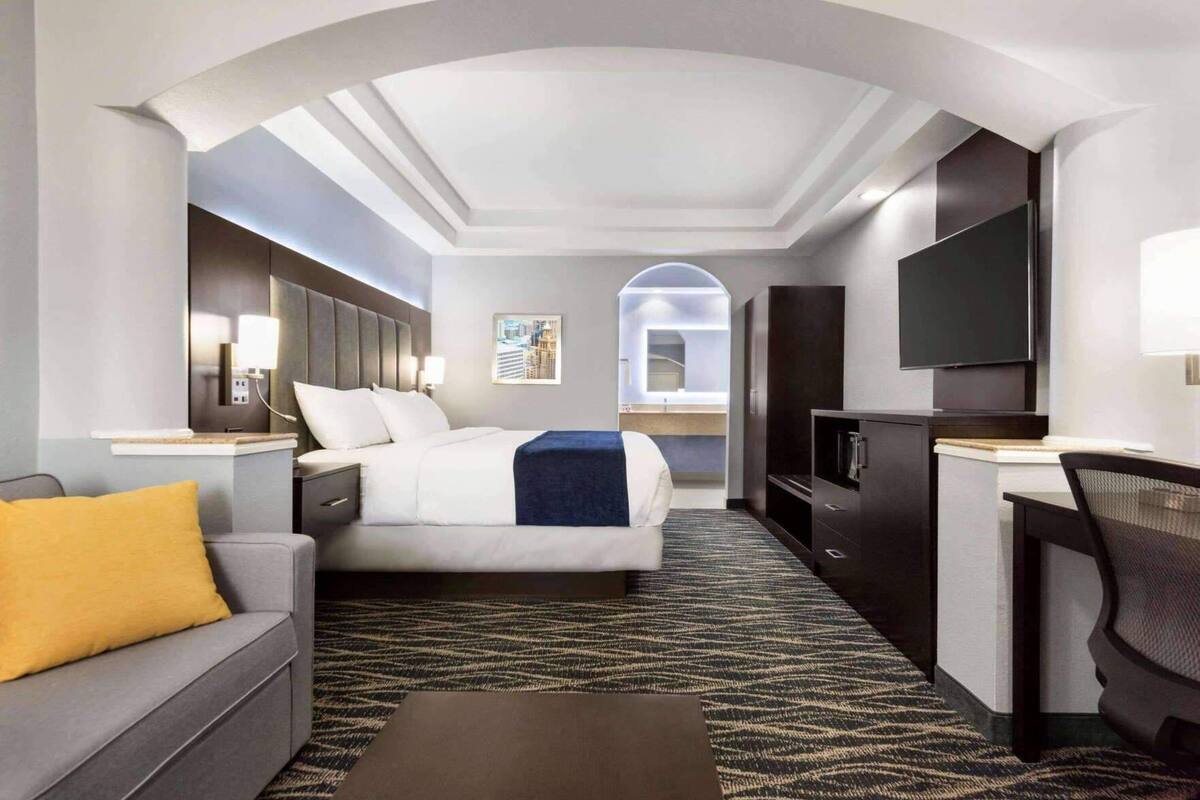Une chambre d’hôtel avec un lit, un bureau, une télévision, un canapé et un miroir.
