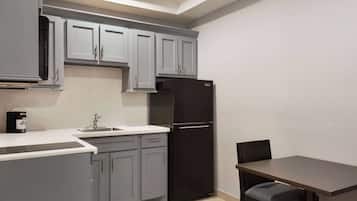 A compact kitchen with grey cabinets, a black refrigerator, a sink, and a dining table with a chair.
