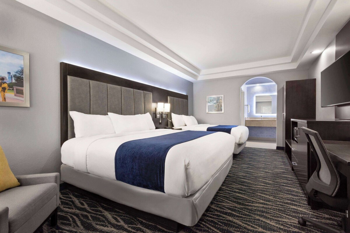 A hotel room with a large bed, a desk, a chair, a TV, and a bathroom visible through an archway.
