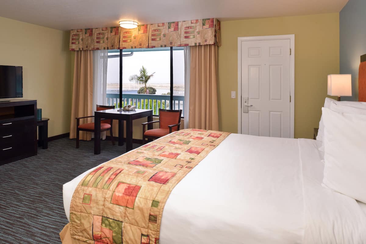 A hotel room with a bed, a desk, a chair, a television, and a view of the beach.