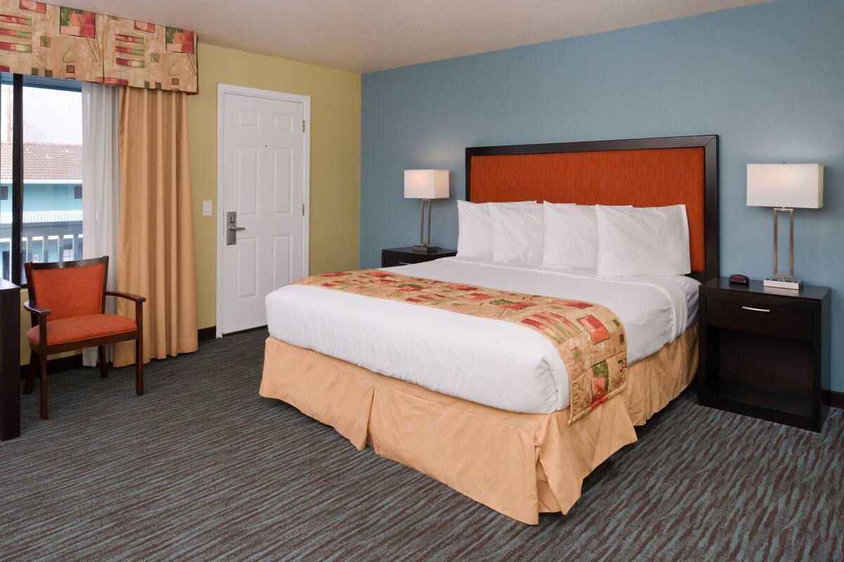 A hotel room with a large bed, two bedside tables with lamps, a chair, and a door.