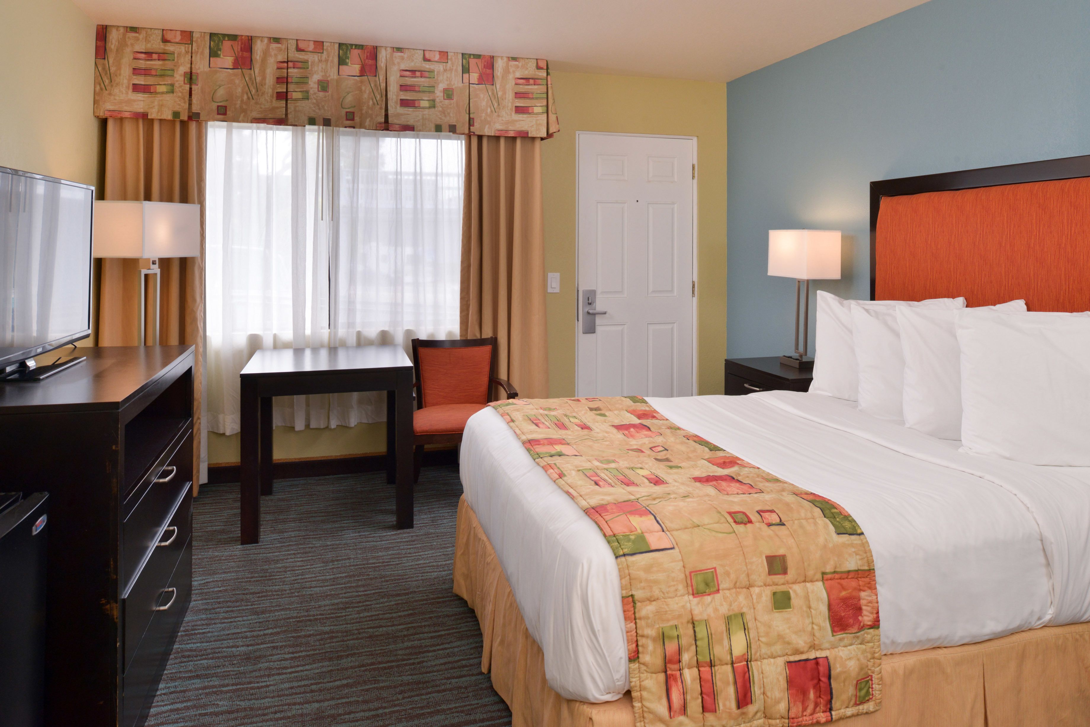 A hotel room with a bed, a desk, a chair, a television, and a door.