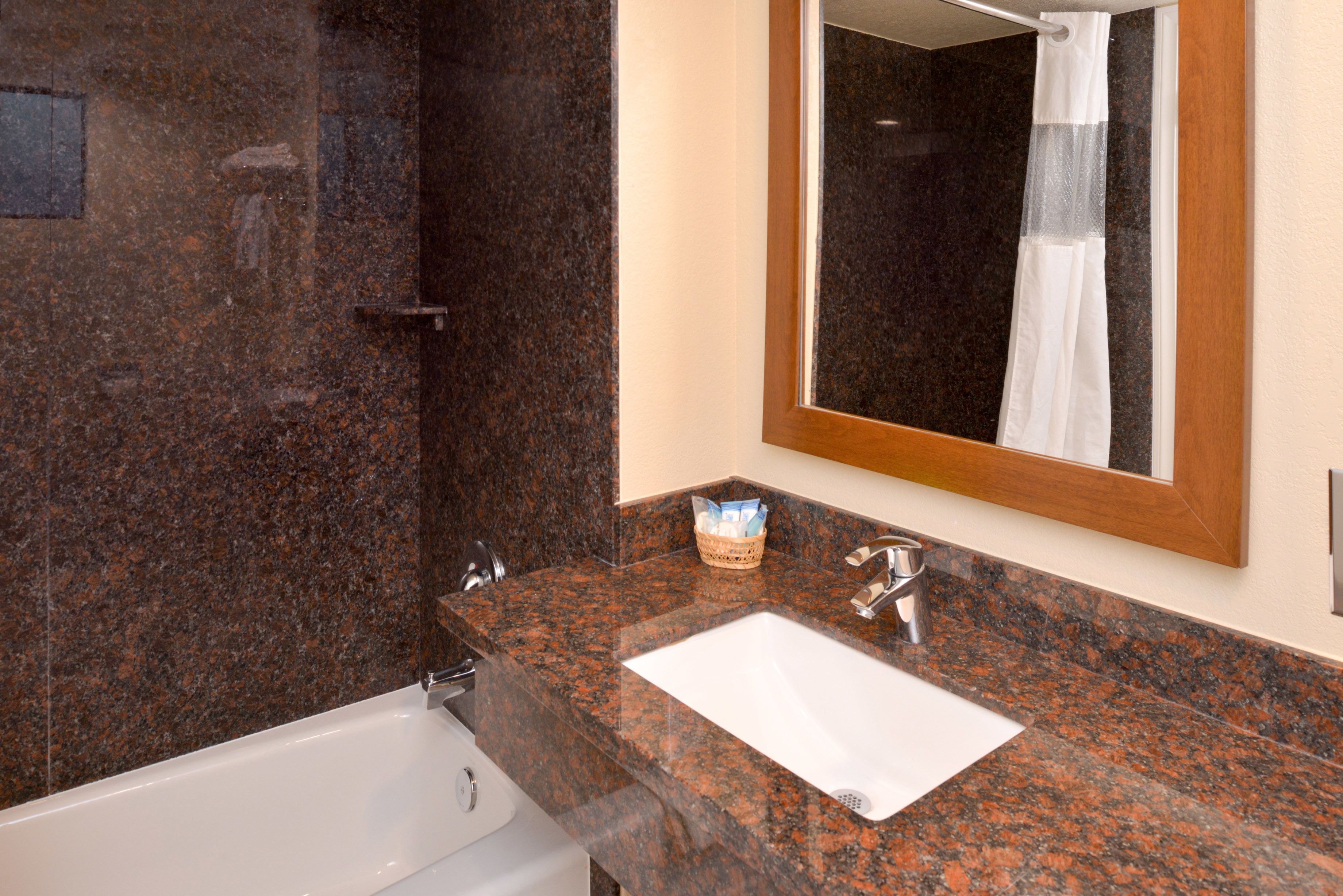 A bathroom with a granite countertop, a white sink, a mirror, and a shower curtain.