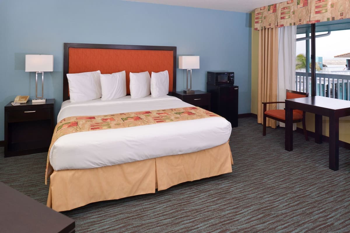 A hotel room with a large bed, two bedside tables, a desk with a chair, a TV, and a window with curtains.