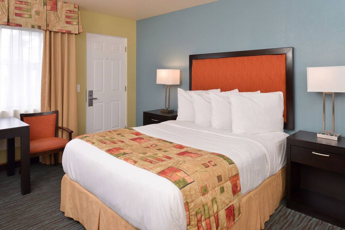 A hotel room with a bed, two bedside tables, a desk, a chair, and a door.