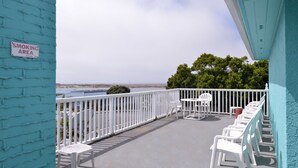 Un balcon avec des chaises blanches et une table, un panneau indiquant un espace réservé aux fumeurs, et une vue sur la plage.