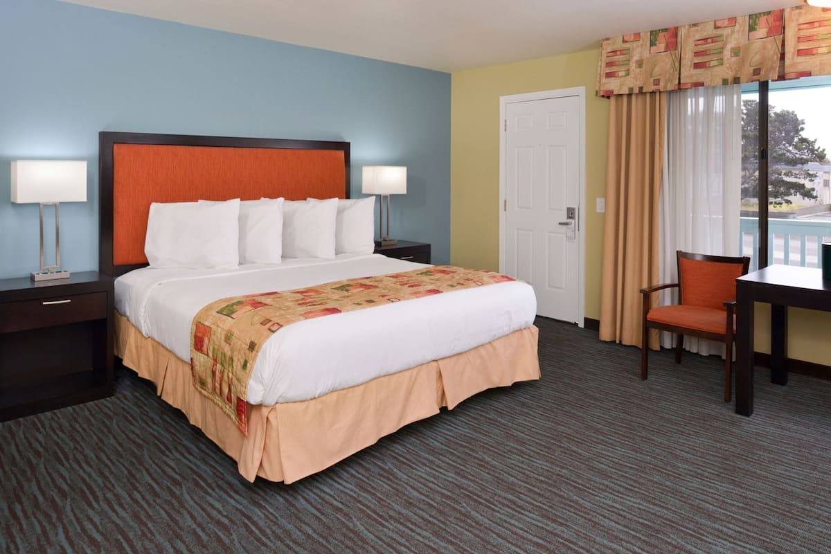 A hotel room with a bed, two bedside tables, a chair, a desk, and a window with curtains.