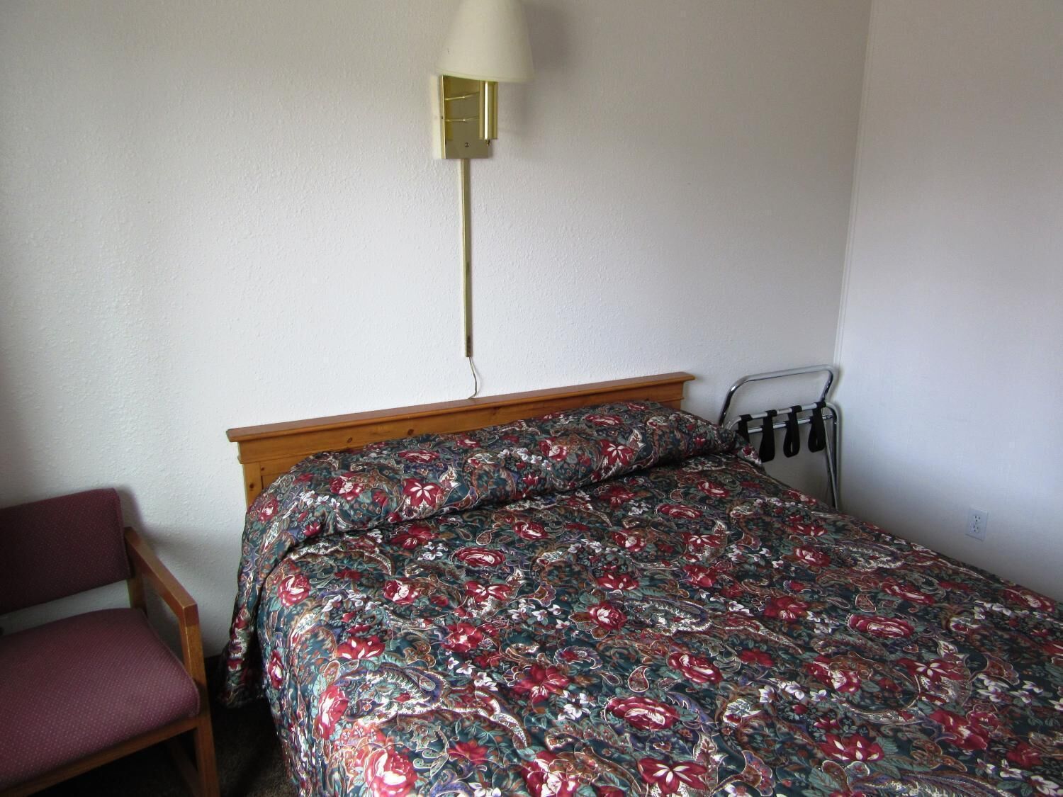 Een kleine, eenvoudige kamer met een bed, een stoel en een lamp.