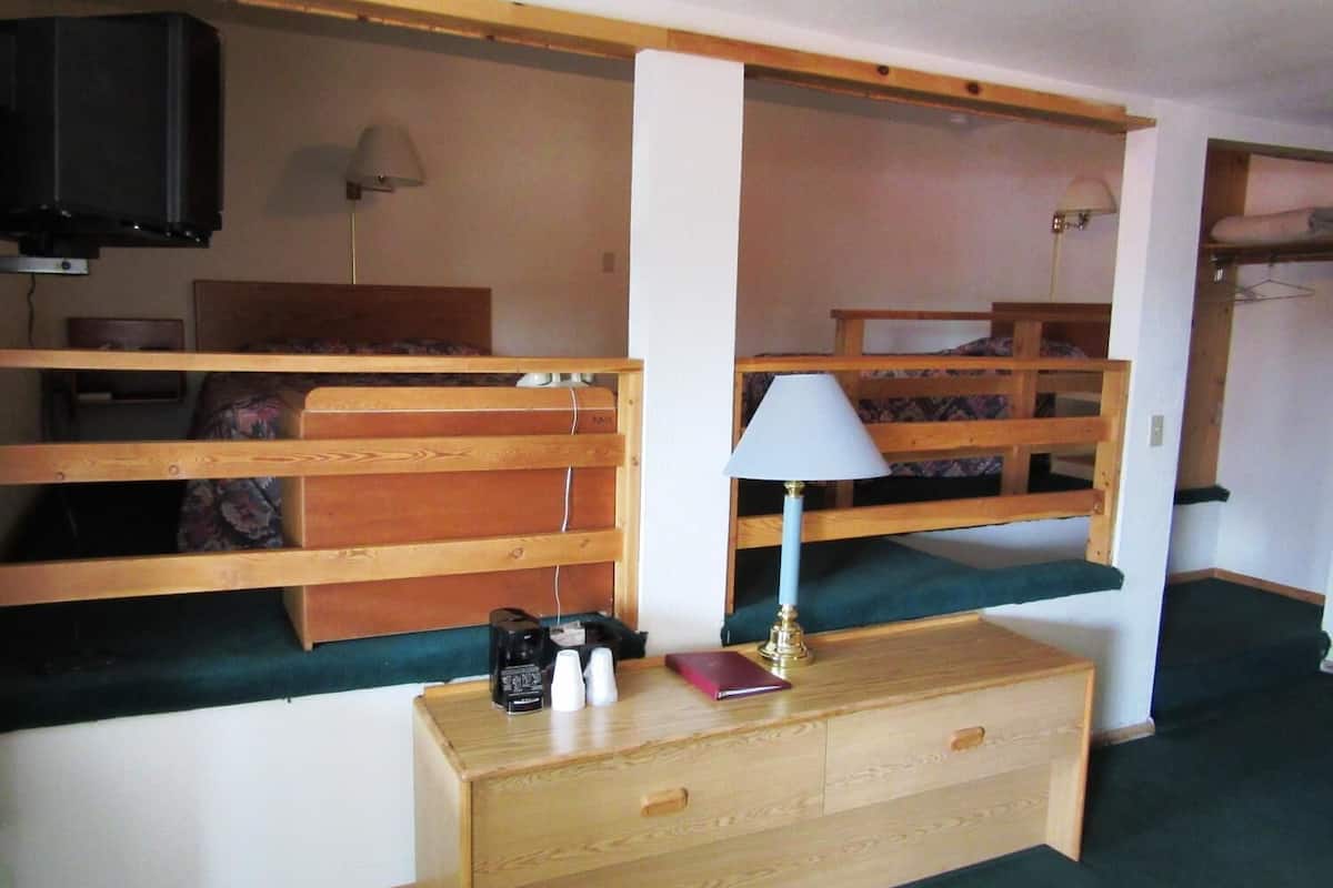 A compact room with bunk beds, a small desk with a lamp, and a television mounted on the wall.