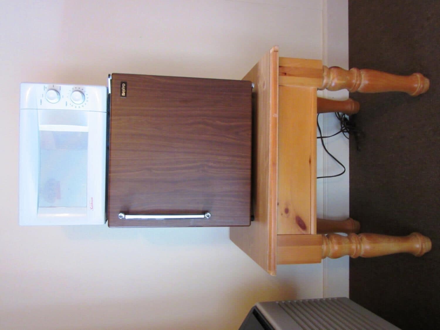 A compact kitchen with a built-in microwave and oven, a wooden table with a power cord, and a radiator below.