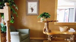 Une pièce comprenant une chaise en bois, une table en bois unique ornée d’une plante, et une tête de cerf encadrée accrochée au mur.