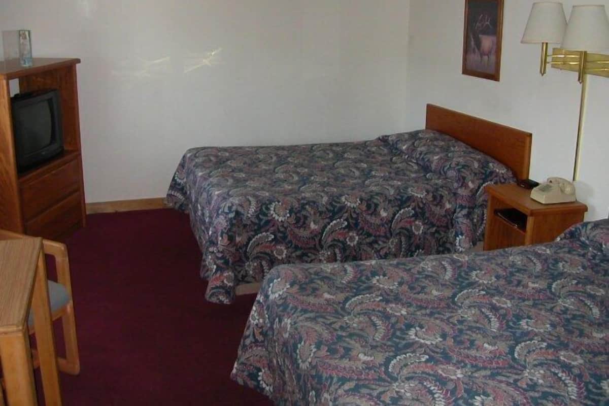 A room with two beds, a wooden nightstand with a lamp, a television on a wooden cabinet, and a framed picture on the wall.
