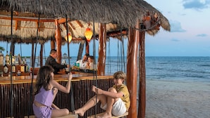 A beach bar with wooden seating and a thatched roof, overlooking the sea.