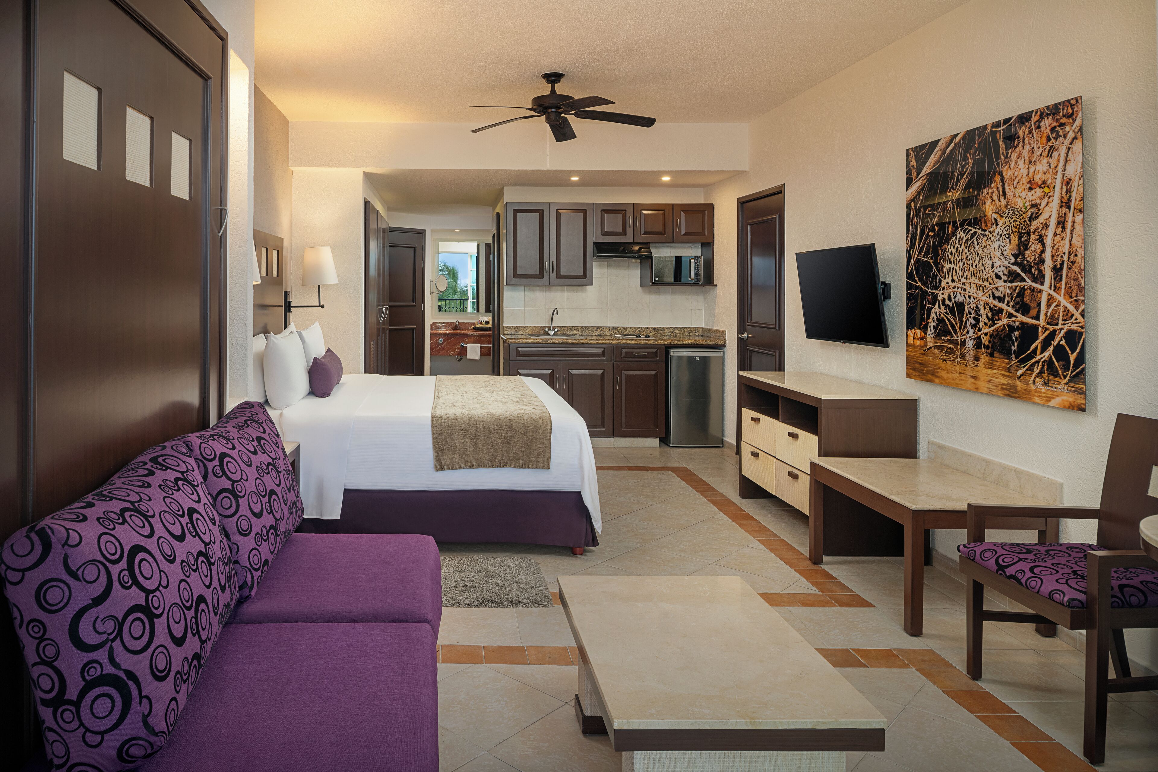 Habitación de hotel con cama, sofá, mesa de comedor, televisor y zona de cocina.