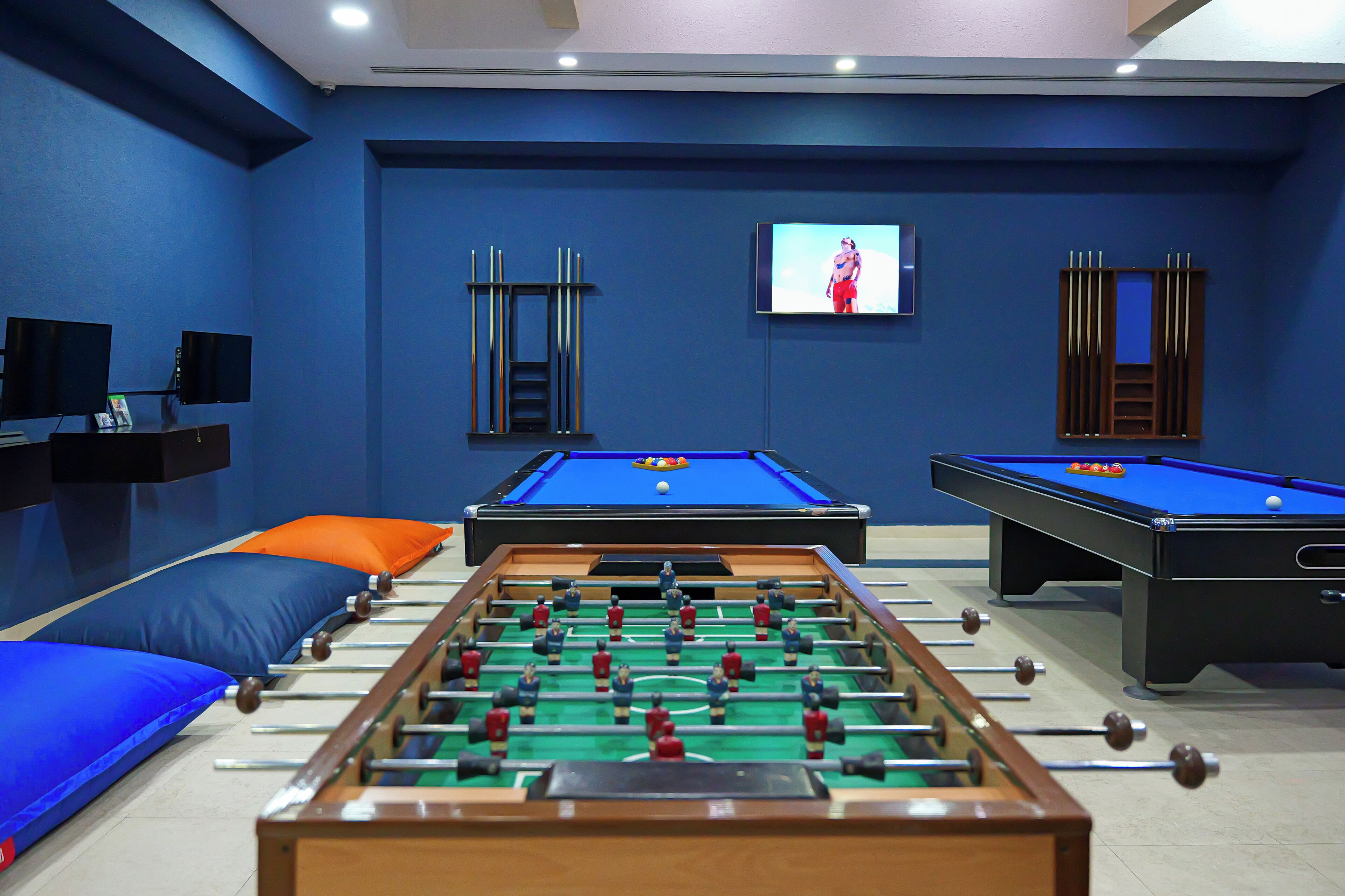 Una mesa de billar, una mesa de futbolín y una pantalla de televisión en una habitación con paredes azules.