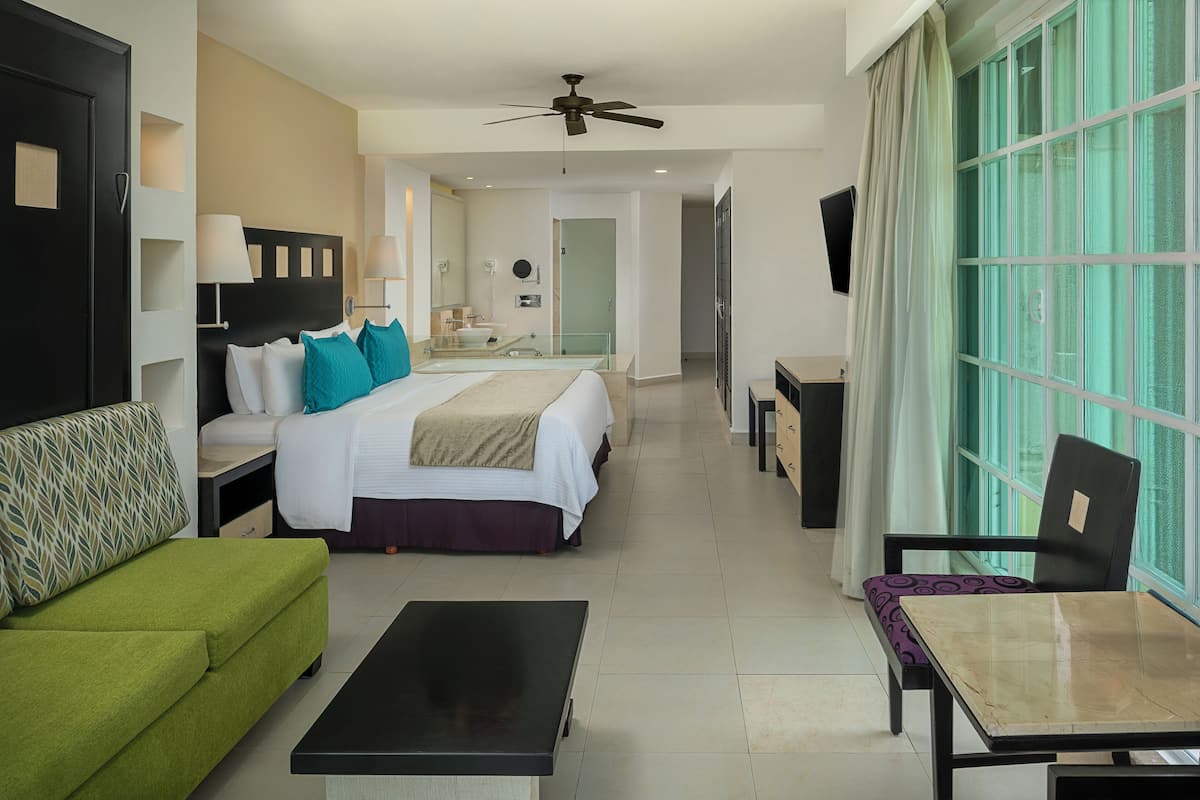 Una habitación de hotel con una cama, un sofá verde, una mesa, una silla, un televisor y una ventana con cortinas.