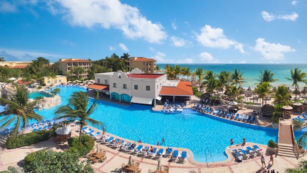A resort with a large swimming pool, palm trees, and a view of the ocean.