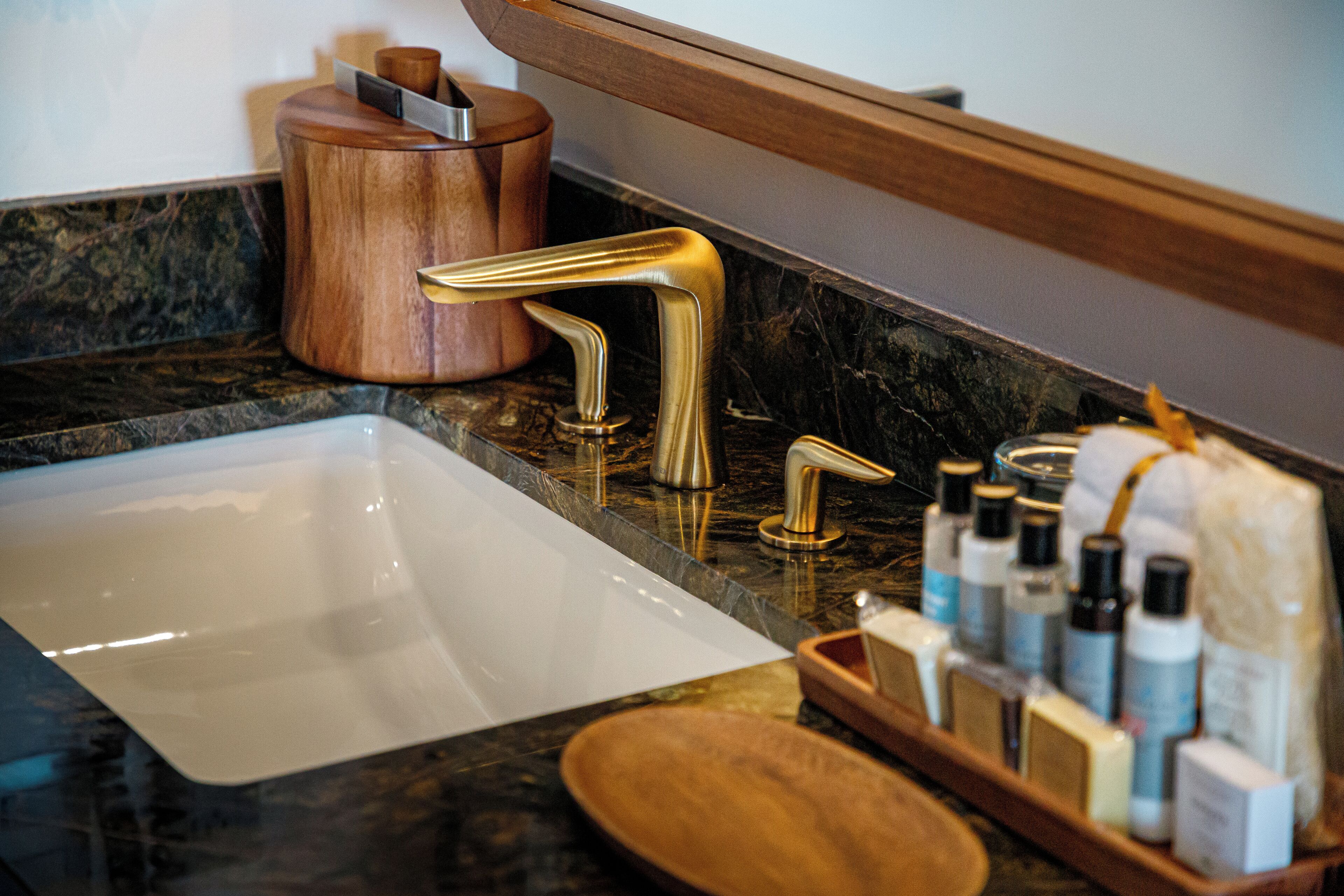 Un baño con encimera de mármol, grifo dorado y jabonera de madera.