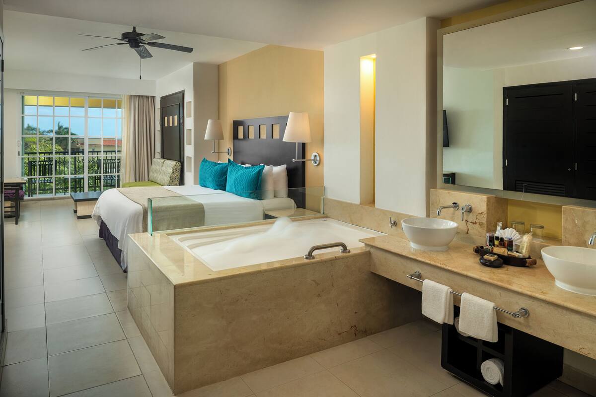Una habitación de hotel moderna con una cama grande, un baño separado con bañera y un balcón con vistas.