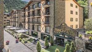 A multi-story hotel with a stone facade, balconies, and a courtyard with outdoor seating.