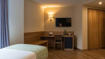 A hotel room with a bed, a desk with a chair, a television, and a wooden wardrobe.