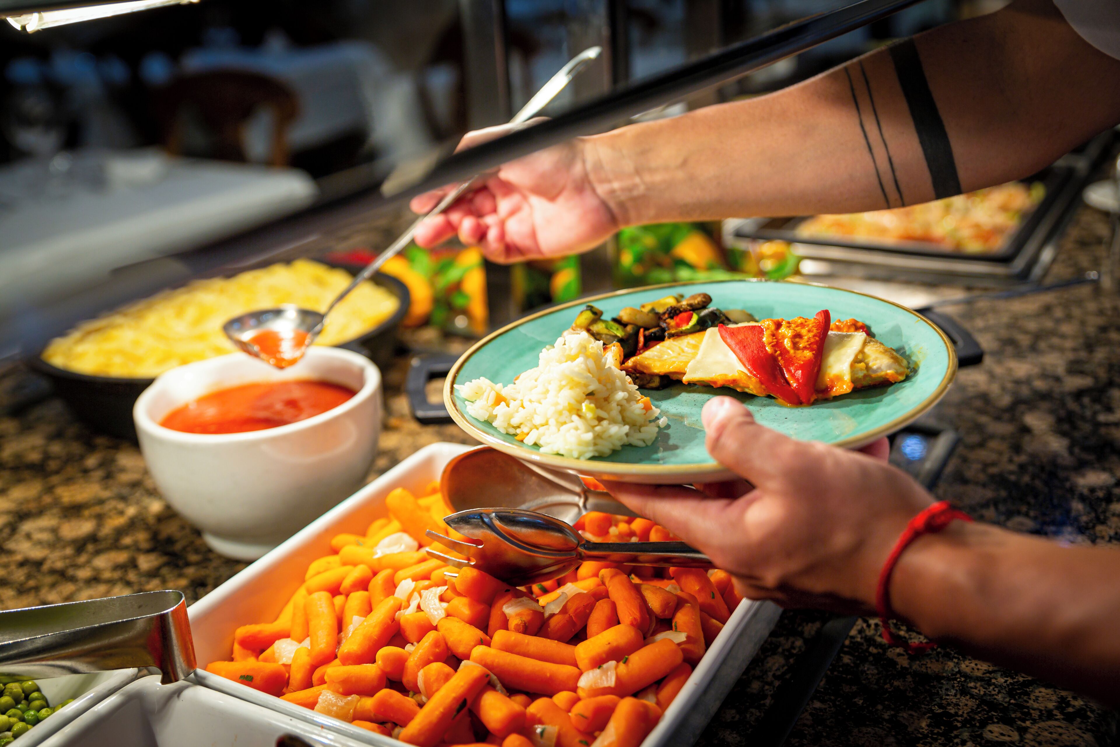 A buffet with various food items including rice, carrots, and a plate with a slice of tomato.