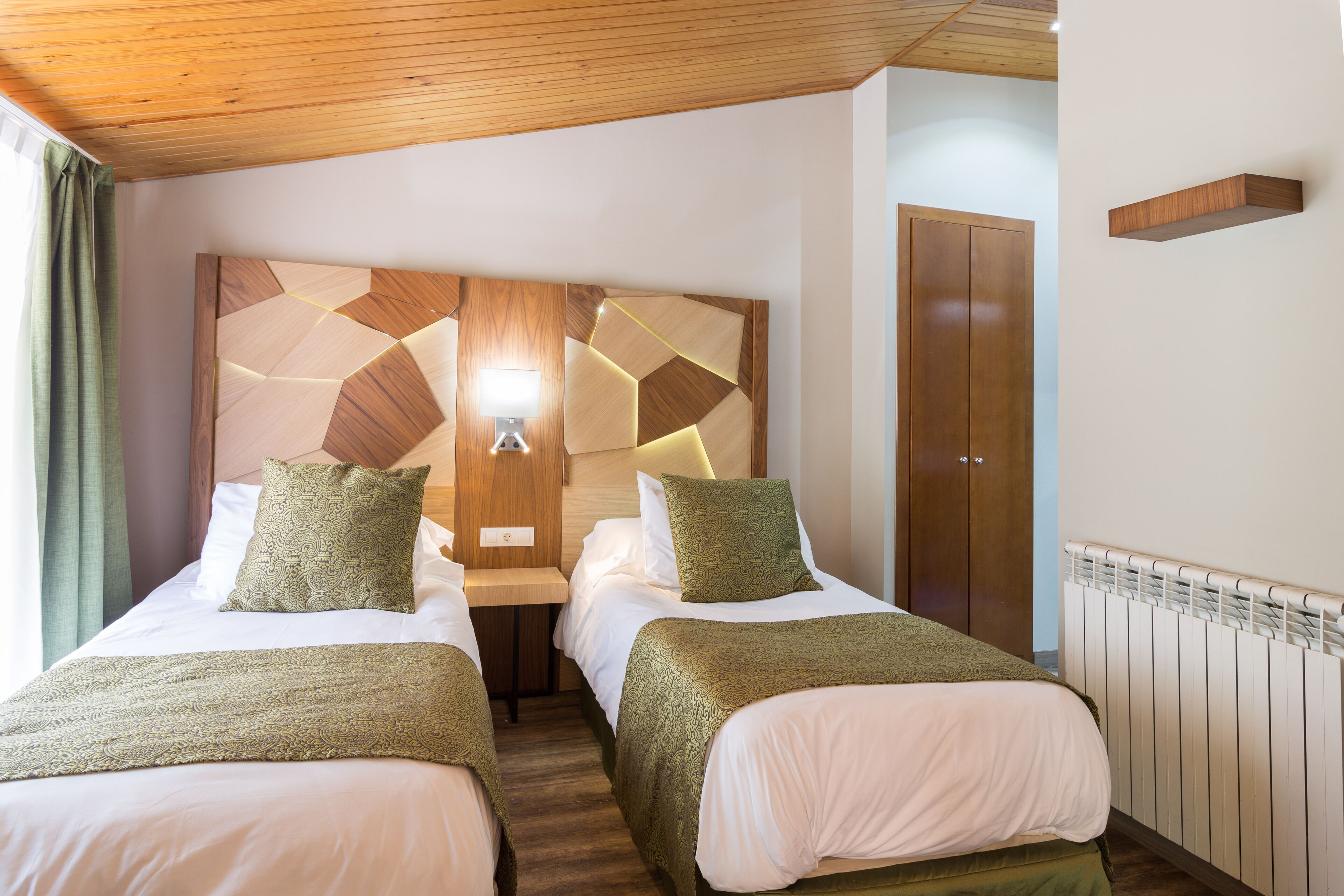 Una habitación de hotel con dos camas, un cabecero de madera, una mesita de noche con lámpara y un armario.