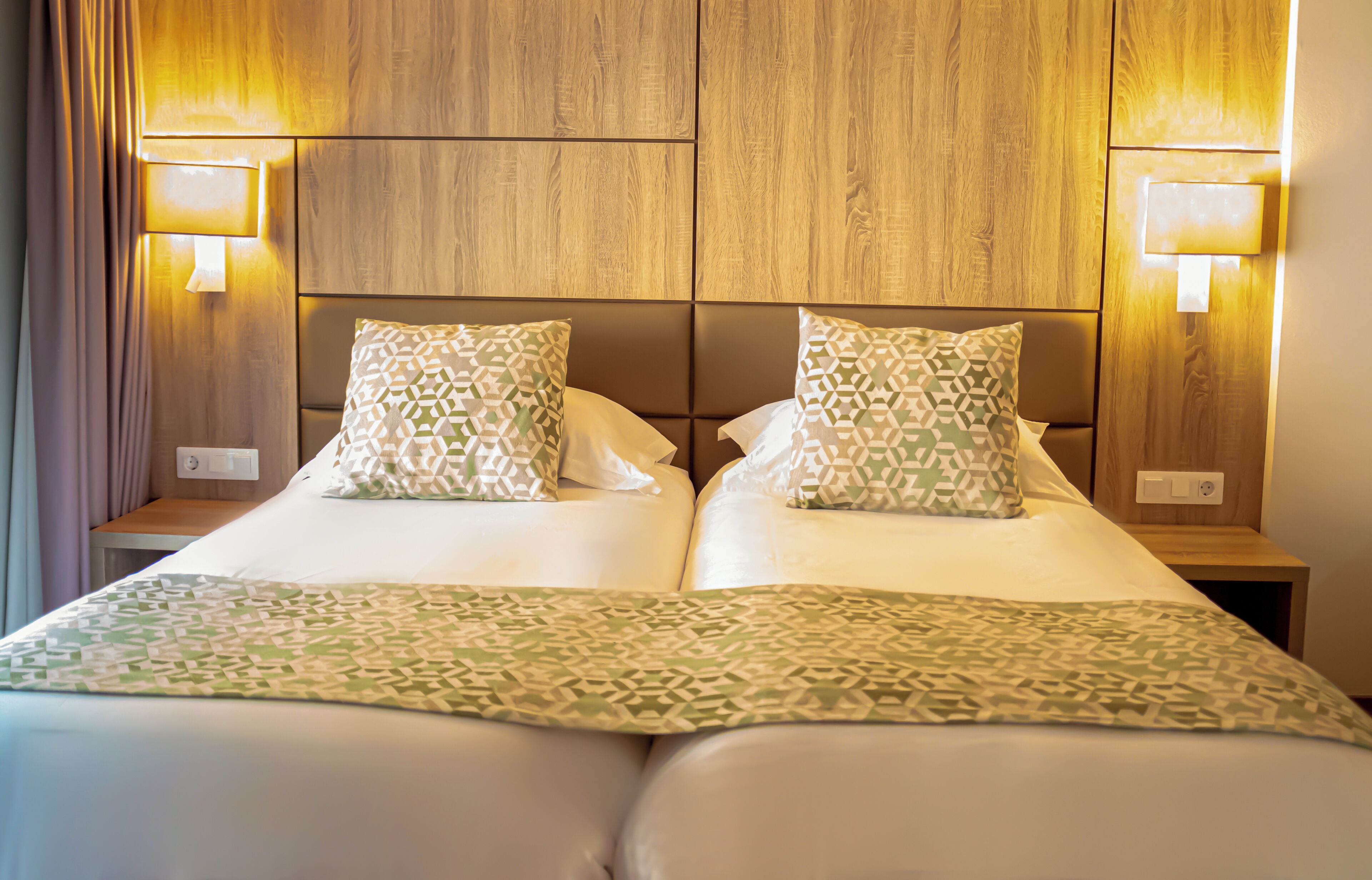 Un lit double avec une couvre-lit et des oreillers à motifs géométriques, une tête de lit en bois et des lampes de chevet.