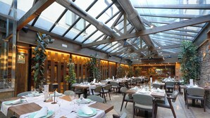 A restaurant with tables set for dining, a glass ceiling, and indoor plants.