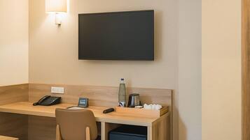 Et hotelværelse med skrivebord, stol, fladskærms-tv, telefon og en lille kaffemaskine.
